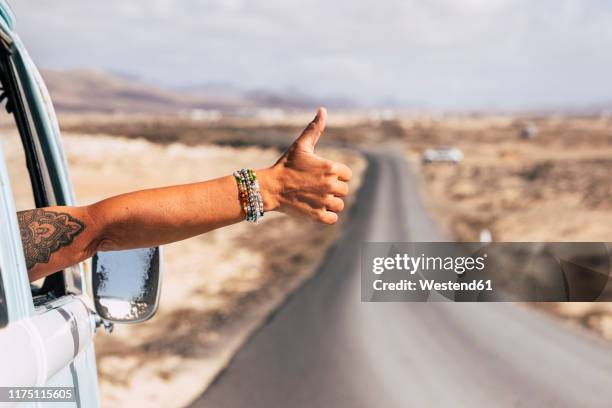 traveller sitting in van, showing thumb up out of the window - tattoo arm stockfoto's en -beelden