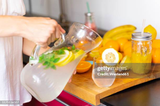 close-up of woman in kitchen at home pouring lemonade into glass - infused water stockfoto's en -beelden