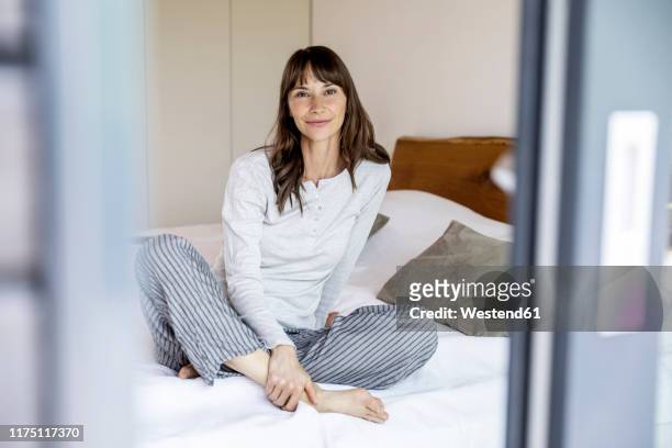 relaxed woman sitting on bed at home - brunette woman bed stockfoto's en -beelden