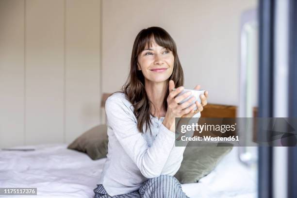 relaxed woman with cup of coffee sitting on bed at home - mirada de reojo fotografías e imágenes de stock
