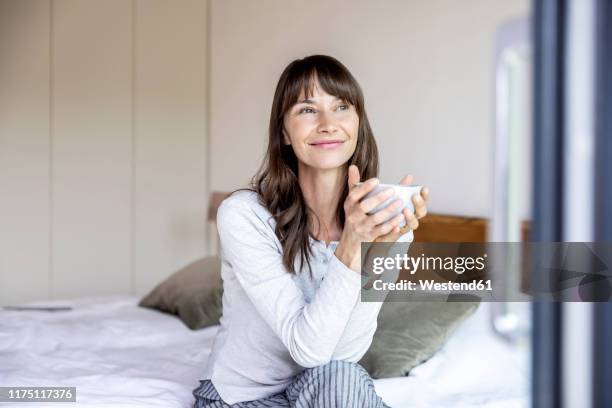 relaxed woman with cup of coffee sitting on bed at home - women drinking coffee photos et images de collection