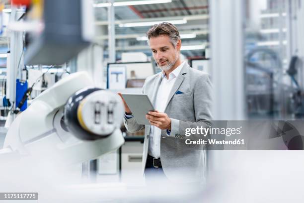 businessman with tablet at assembly robot in a factory - rechnerunterstützte fertigung stock-fotos und bilder
