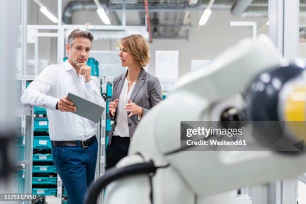 businesswoman and man with tablet talking at assembly robot in a factory - rechnerunterstützte fertigung stock-fotos und bilder