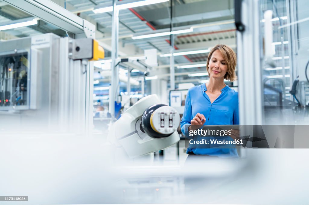 Businesswoman with tablet at assembly robot in a factory
