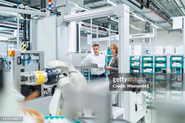 businesswoman and manwith tablet talking in a modern factory - rechnerunterstützte fertigung stock-fotos und bilder