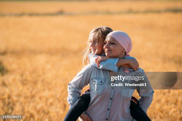 a woman with cancer carrying her daughter on her back, looking sideways - cancerland 2019 bildbanksfoton och bilder