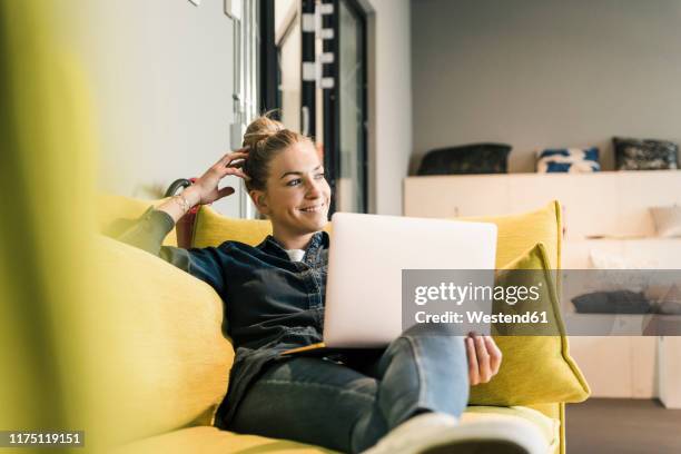 casual businesswoman using laptop on couch in office lounge - businesswoman couch fotografías e imágenes de stock