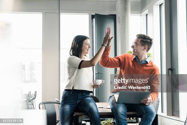 happy casual businessman and woman high fiving in office - high five business stock-fotos und bilder