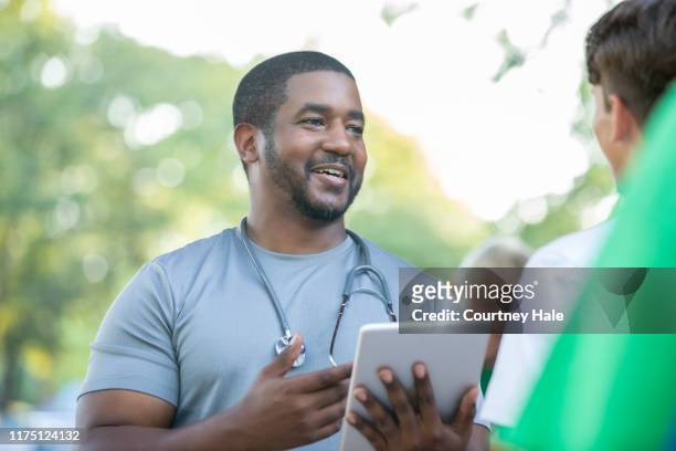 doctor praat met communitylid tijdens outdoor health fair - male volunteer stockfoto's en -beelden