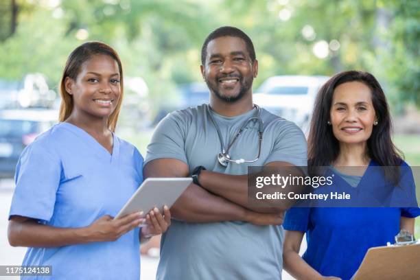 diverse medical team of doctors and nurses smile during outdoor health fair for local community - doctor reaching stock pictures, royalty-free photos & images
