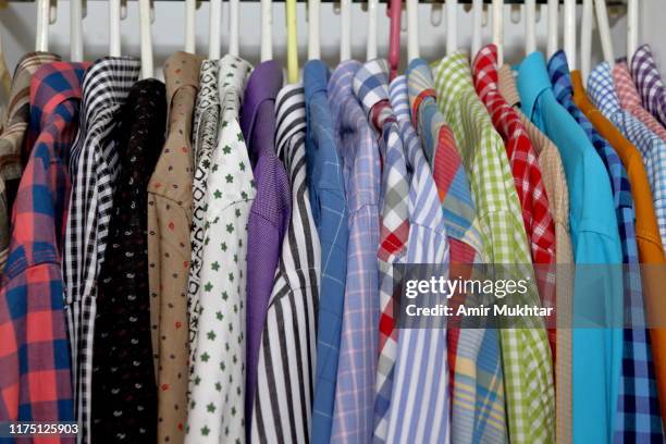 shirts hanging on hangers in closet - multi coloured shirt stock-fotos und bilder