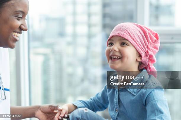 female doctor sits with child patient fighting cancer - bald girl stock pictures, royalty-free photos & images