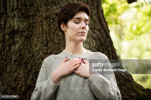 woman practising reiki, large tree trunk in background - hands on chest stock pictures, royalty-free photos & images