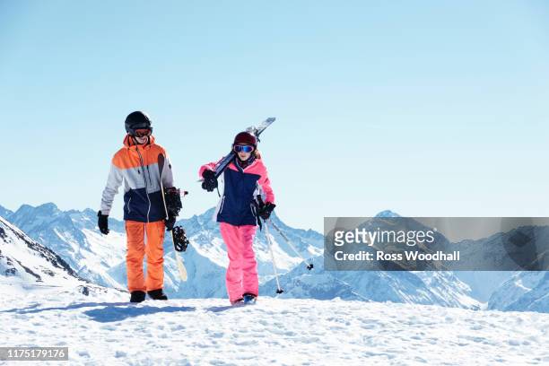 teenage boy snowboarder with sister skier walking on snow covered mountain top,  alpe-d'huez, rhone-alpes, france - アルプデュエーズ ストックフォトと画像