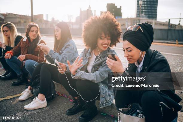 friends sitting on kerb using smartphone, milan, italy - digital natives stock-fotos und bilder