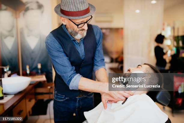 hairdresser shaving customer's beard in barber shop - barber shop 3 stock pictures, royalty-free photos & images