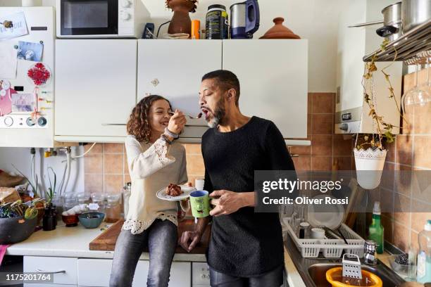 daughter sharing a piece of cake with father in kitchen at home - eating cake stockfoto's en -beelden