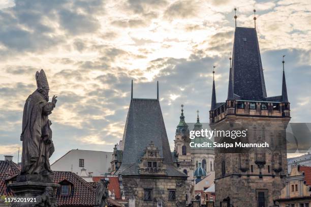statue of st. adalbert on charles bridge and the lesser town bridge tower with dome of st. nicholas church on background - st nicholas cathedral stock-fotos und bilder