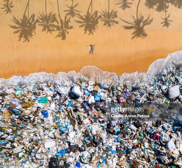 man lying on the beach with garbage in the water. ocean pollution concept with plastic and garbage - plastic pollution beach stock pictures, royalty-free photos & images