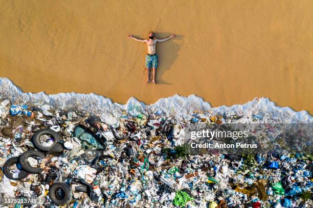 man lying on the beach with garbage in the water. ocean pollution concept with plastic and garbage - garbage man stockfoto's en -beelden