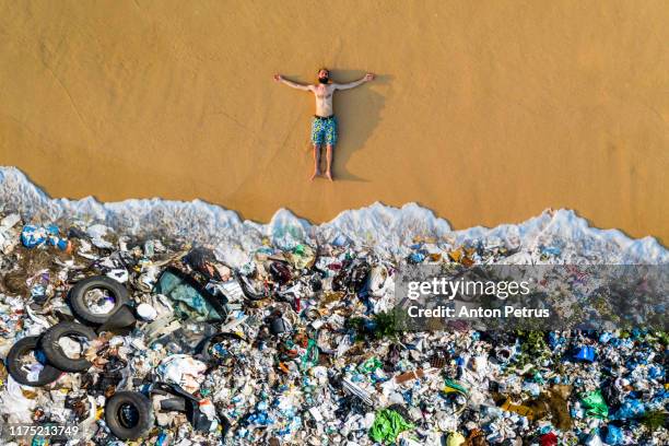 man lying on the beach with garbage in the water. ocean pollution concept with plastic and garbage - water pollution stock pictures, royalty-free photos & images