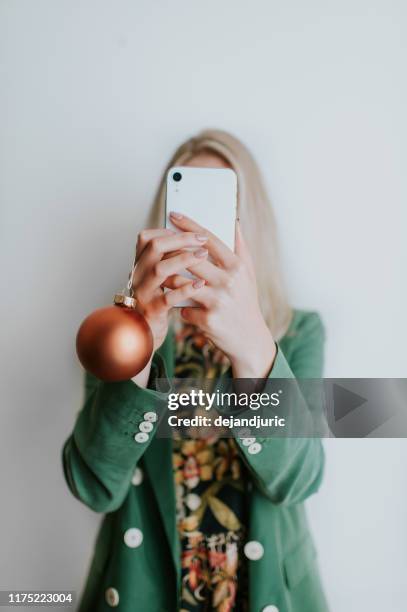 woman holding a christmas bauble and taking a selfie - obscured face phone stock pictures, royalty-free photos & images