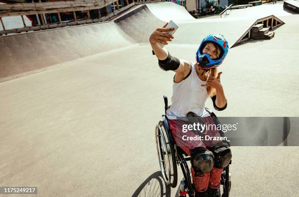 disabled woman in wheelchair doing stunts in skate park and taking selfie - disabled extreme sports stock pictures, royalty-free photos & images