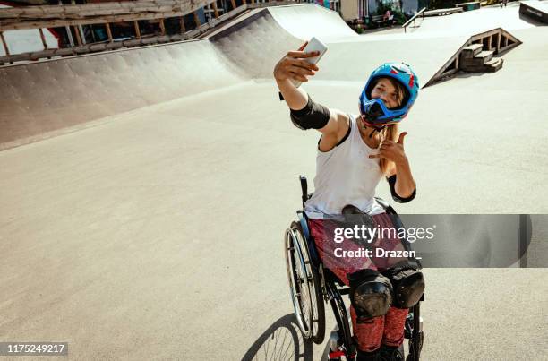 disabled woman in wheelchair doing stunts in skate park and taking selfie - daredevils and stunts imagens e fotografias de stock