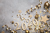 Holiday background with golden Christmas decorations and New year 2020 numbers and confetti stars top view.