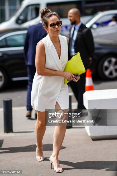 Guest wears earrings, tortoise-shell pattern sunglasses, necklaces, a neon-green clutch, a white wrap-over mini dress , transparent vinyl heeled...