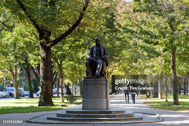 Couple strolling in Commonwealth Avenue Mall near William Lloyd Garrison statue sculpted by Olin Levi Warner, in Boston, United States.