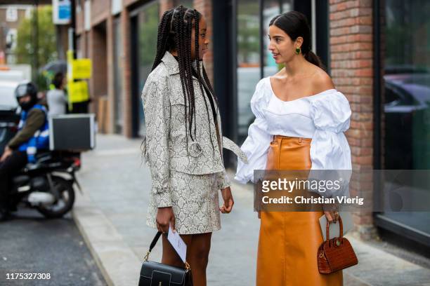 Chrissy Rutherford wearing skirt and jacket with snake print and Bettina Looney is seen wearing white blouse with wide sleeves, orange high waist...