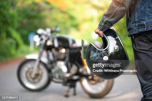 handsome man in jean is holding a helmet and vintage motorcycle blur background - motor ストックフォトと画像