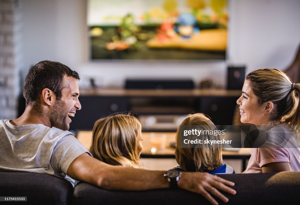 Gelukkige ouders praten terwijl ze thuis TV kijken met hun kinderen.