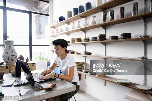 young asian entrepreneur working from her laptop in her store - computer store stockfoto's en -beelden