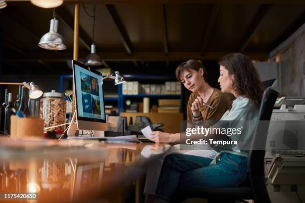 two creatives sharing a computer and doing paper work. - design studio stock pictures, royalty-free photos & images