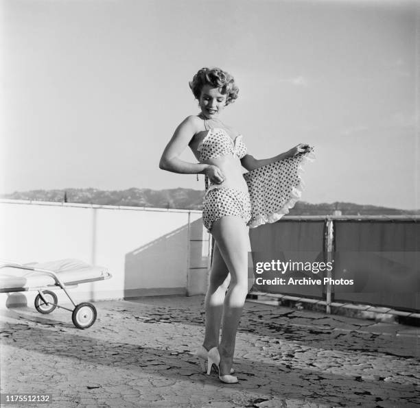 American actress Marilyn Monroe wearing polka dot bikini with matching wraparound miniskirt and heels during a photo shoot on a rooftop, circa 1951.