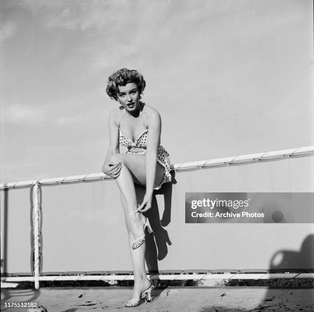 American actress Marilyn Monroe , wearing a polka dot bikini, fastens a heeled sandal during a photo shoot on a rooftop, circa 1951.