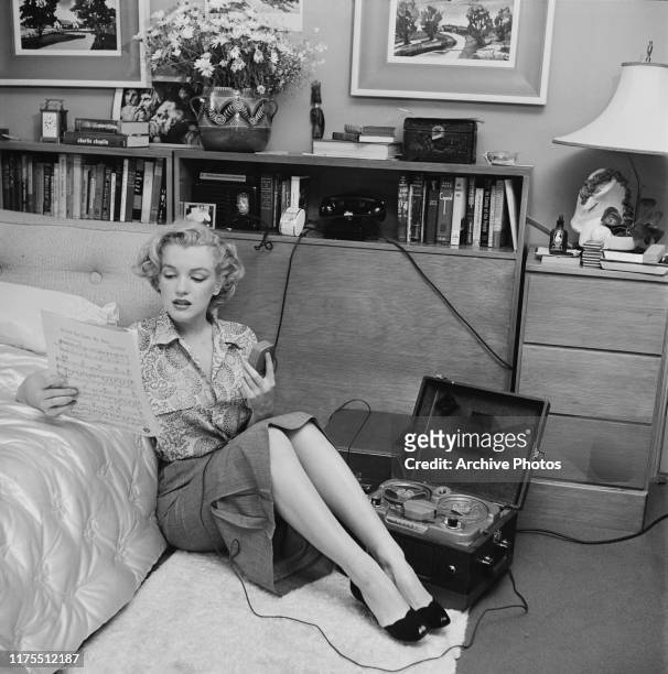 American actress Marilyn Monroe reading sheet music while sitting on a bedroom floor with a tape player on the side, US, circa 1950.