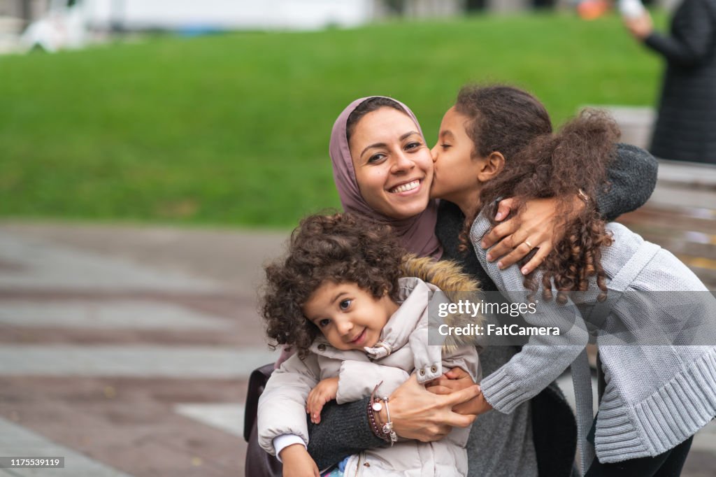 Muslim mother hugging daughters in city park