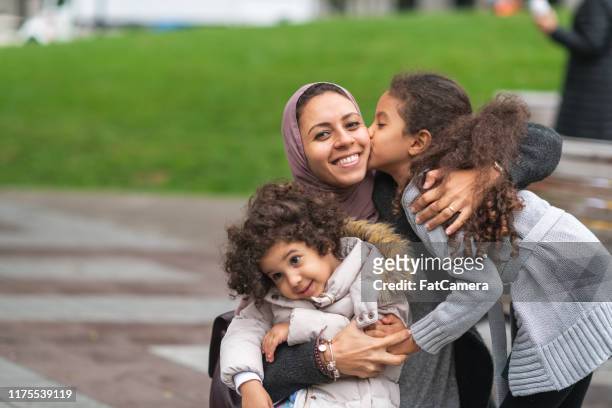 muslim mother hugging daughters in city park - emigration and immigration stock pictures, royalty-free photos & images