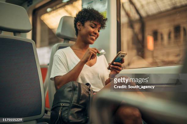 Woman in train using phone and credit card for shopping online