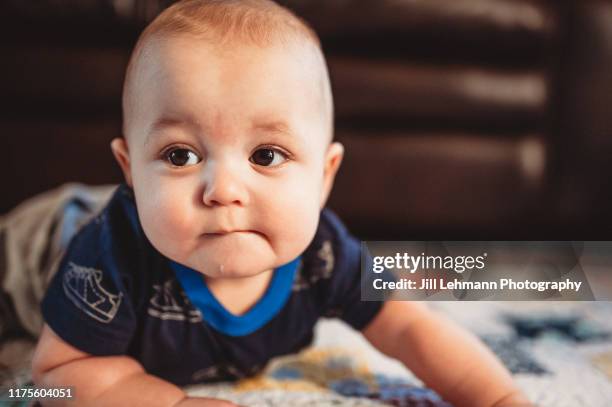 adorable and cute 6 month old baby boy does tummy time in living room on a blanket - bébé grimace photos et images de collection
