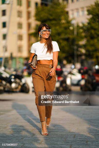 Carlotta Rubaltelli wears fringed and glitter glasses, a white cropped t-shirt, a bag, brown pants, shoes, outside the Alberta Ferretti show during...