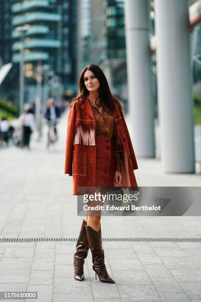 Paola Turani wears a brown suede jacket with fringes, a brown silky lustrous shirt, a leather skirt, leather high boots, outside the Alberta Ferretti...