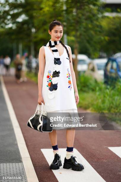 Guan Xiaotong wears a black and white scarf, a long dress with colored floral prints, a black and white bag, , outside the Prada show during Milan...