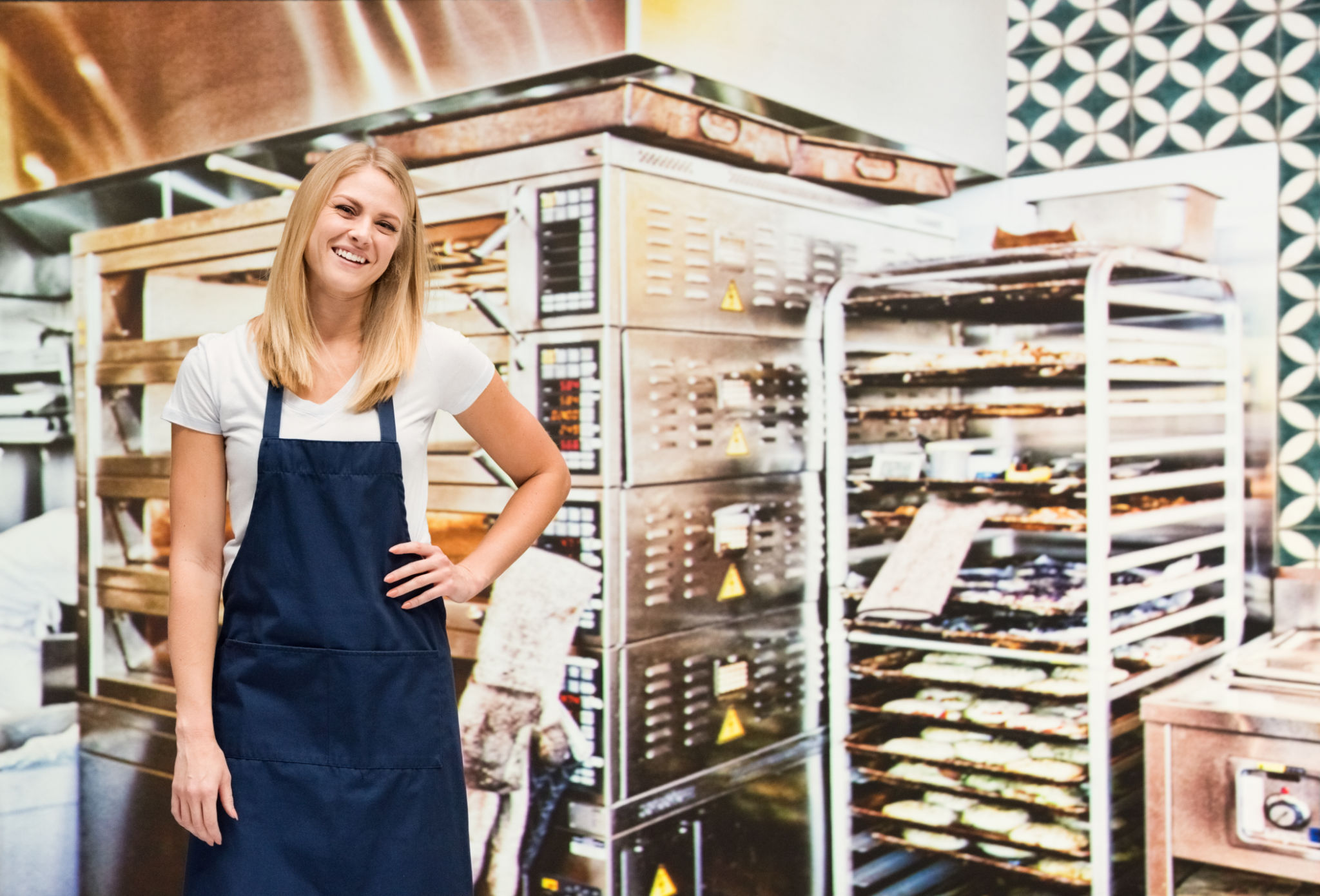 One person / waist up of blond hair caucasian female / young women baker / caterer / retail occupation cooking / preparing food / standing at the bakery / restaurant in the store wearing apron / uniform / t-shirt / shirt and celebration / retail One person / waist up of blond hair caucasian female / young women baker / caterer / retail occupation cooking / preparing food / standing at the bakery / restaurant in the store wearing apron / uniform / t-shirt / shirt and celebration / retail