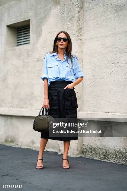 Chloe Harrouche wears sunglasses, a blue shirt, a black skirt with cargo pockets, a Prada green khaki bag, outside the Prada show during Milan...