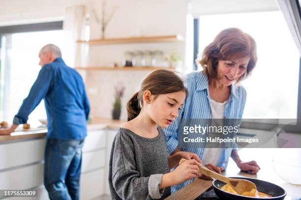 senior grandparents and granddaughter preparing food indoors in kitchen. - granny flat stock pictures, royalty-free photos & images