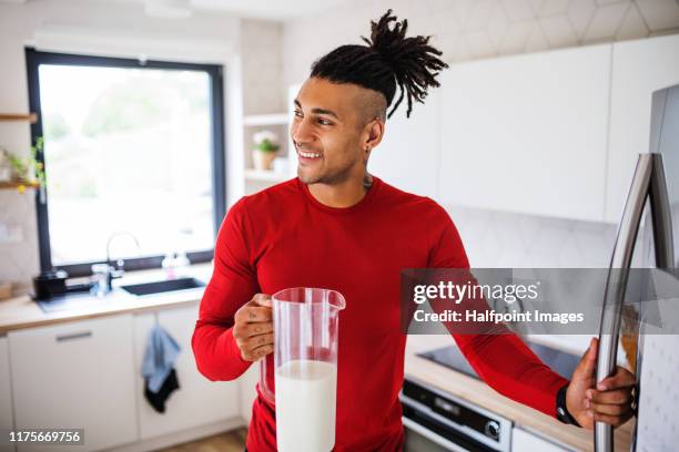 a portrait of fit mixed race man getting milk from fridge after doing exercise at home. - calcio sport imagens e fotografias de stock